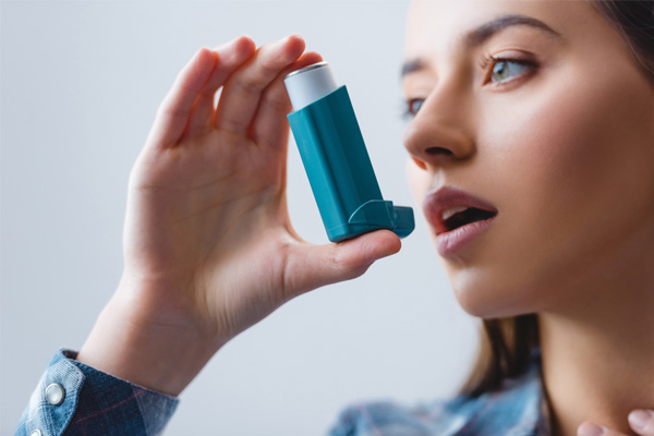 Close-up view of young woman with asthma using inhaler depicting indoor air pollution