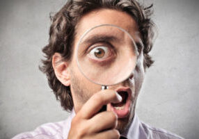 close up of a man looking through a magnifying glass depicting top signs of poor indoor air quality