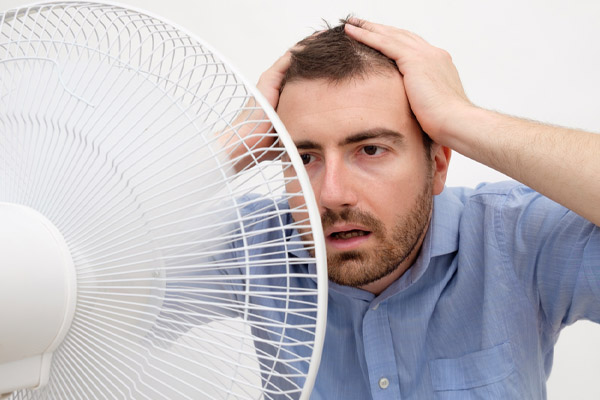 flushed man feeling hot in front of a fan due to poor ac performance