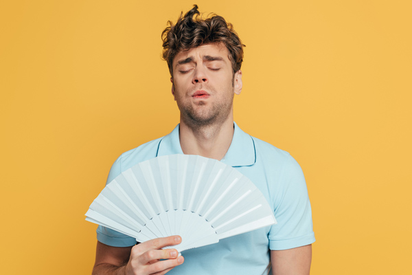 man cooling himself with a fan due to mismatched air conditioner