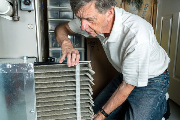 senior man changing a dirty air filter in an hvac furnace