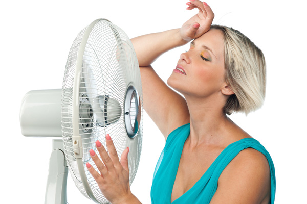 woman cooling herself with a fan due to broken air conditioner